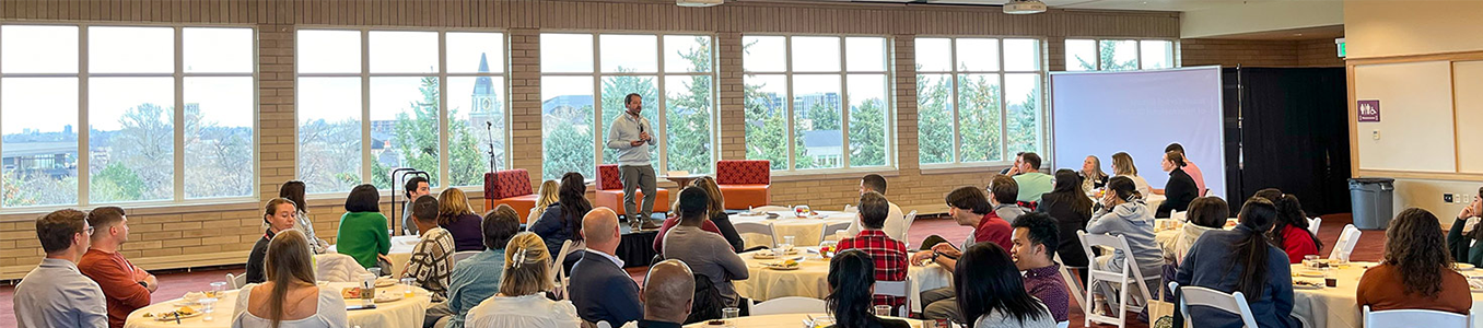 Event with several people around 6 tables with a guest speaker